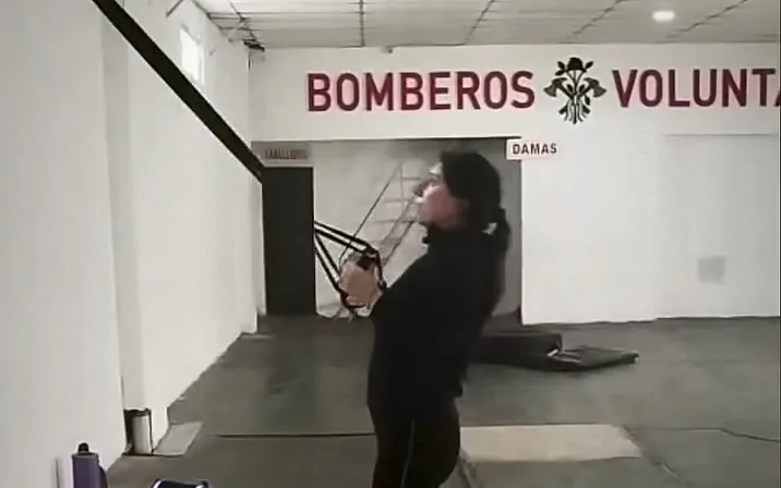 Una alumna hace remo con TRX en el salón del cuartel, debajo del letrero de Bomberos Voluntarios.