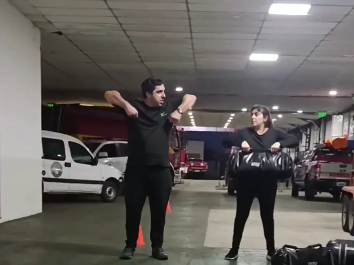 Nicolás Valle le muestra un ejercicio a una alumna en el Cuartel de Bomberos, con las autobombas estacionadas atrás.